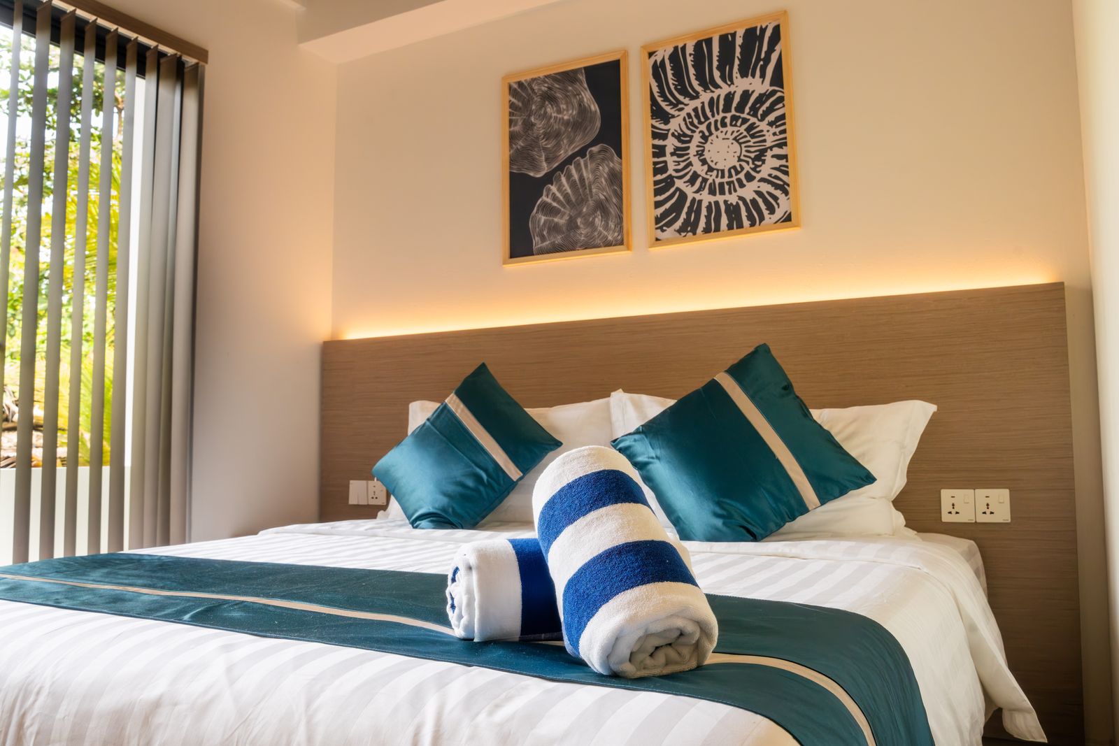 Deluxe room bed with teal cushions and rolled beach towels
